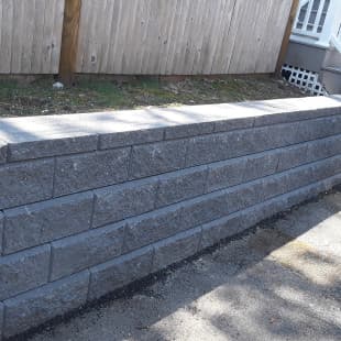 A neatly constructed gray brick retaining wall with a wooden fence in the background.